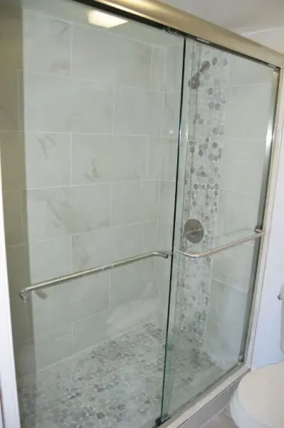 Walk-in shower with large-format marble-look tile, mosaic accent strip and sliding glass door