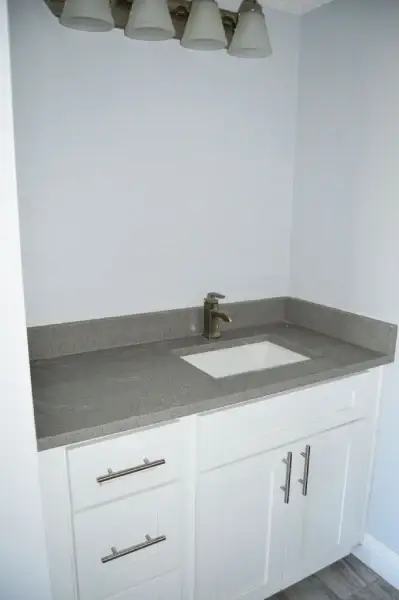 Compact white vanity with gray quartz top and undermount sink in a remodeled bathroom
