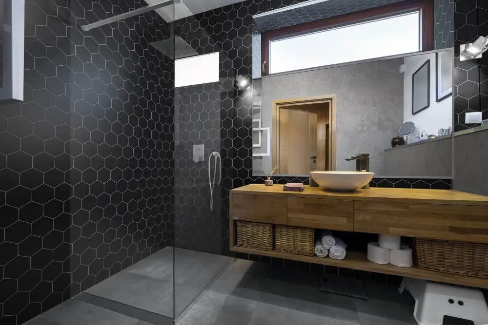 Curbless walk-in shower with dark hexagon tile, glass panel and a floating wood vanity