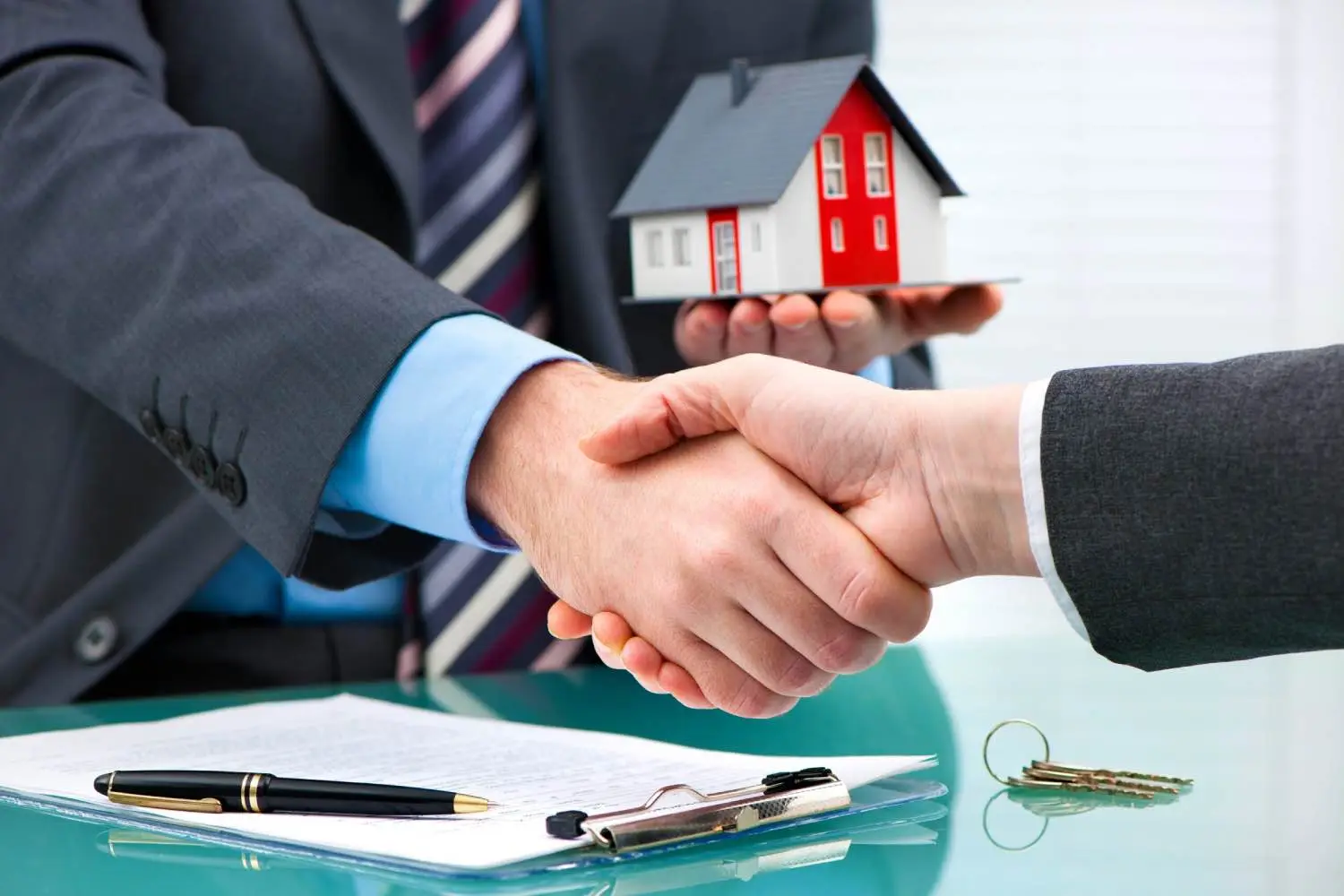 Homeowner and contractor shaking hands over a signed agreement with house keys on the table