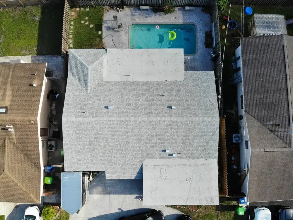 Aerial view of a two-section roof replacement with dumpster staged on the driveway