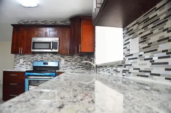 Dark wood kitchen cabinets with granite countertops and a glass mosaic tile backsplash