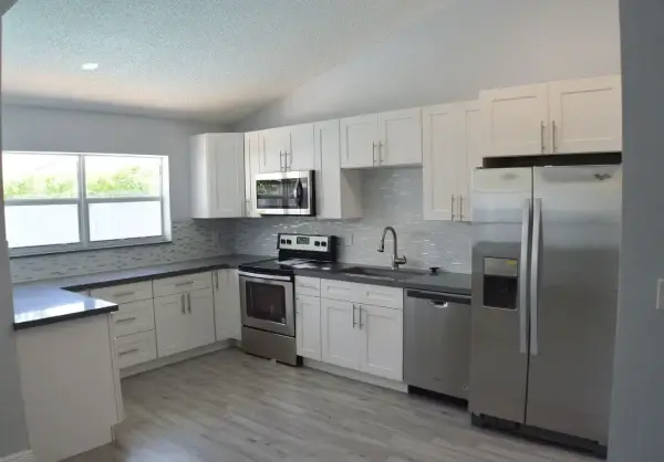 White shaker kitchen with dark countertops, tile backsplash and stainless appliances after a full remodel